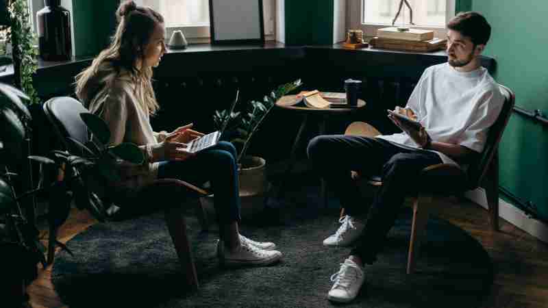 A man and woman engaged in conversation at a stylish, plant-filled home office with modern furniture and digital devices., tags: ruolo dell'ia nella terapia di - pexel
