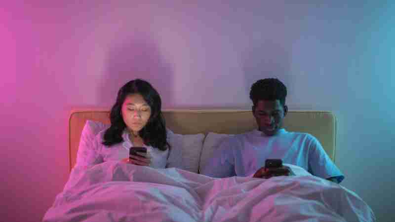 Couple lying in bed using smartphones under colored lights, showcasing modern digital lifestyle., tags: di - pexel